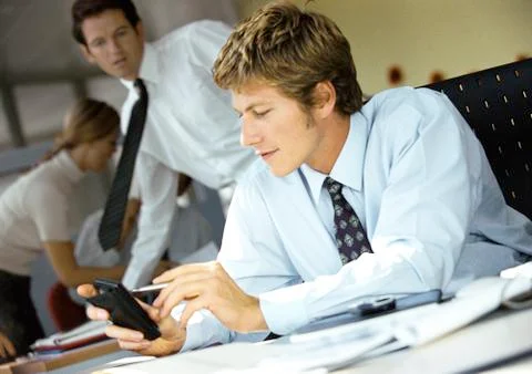 Young businessman using pocket computer, colleagues in background. Stock Photos