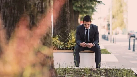 Young Businessman Using Smartphone While Sitting At Bench Stock Footage 87404996