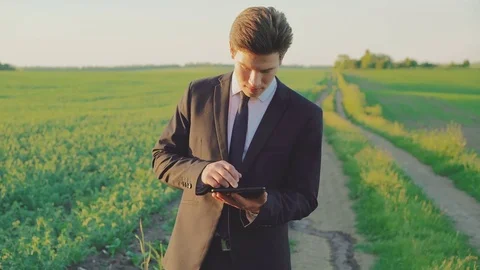 Young businessman using tablet on the green field on the sunset 4K Stock Footage