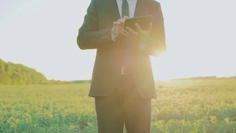 Young businessman using tablet on the green field on the sunset 4K 動画素材 76997820