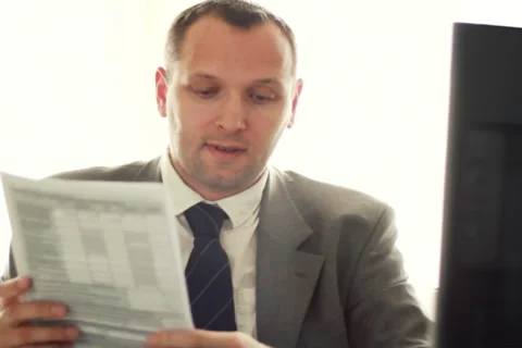 Young businessman working on computer and looking into documents NTSC 스톡 동영상 4425736
