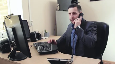 Young businessman working on computer in office answers a phone call Stock Footage 84492866