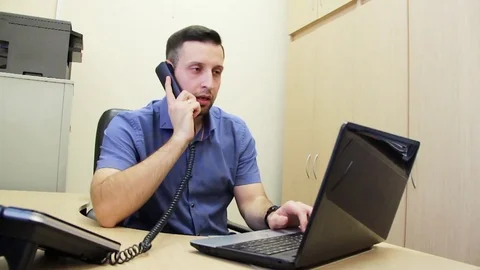 Young businessman working on laptop computer in office answers a phone call Stock Footage 84492902