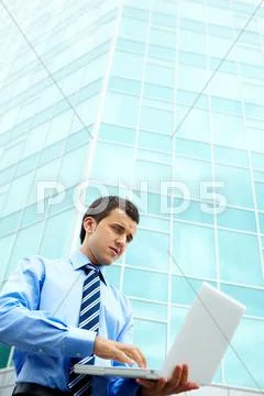 Young businessman working with laptop by office building Stock Photos