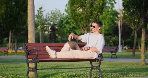 A young businessman working on a laptop while lying on a park bench Stock Footage 305873969