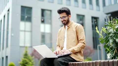 Young businessman works on a laptop while sitting on a bench near the office  Stock Footage 246995285