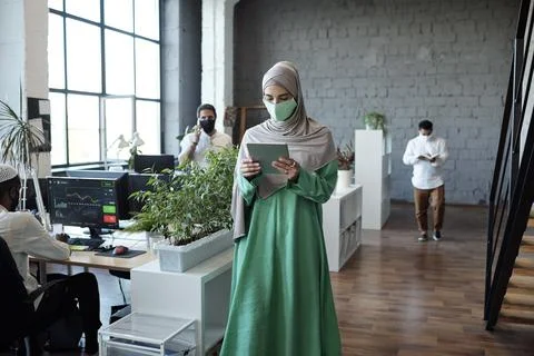 Young businesswoman in hijab walking along tables in large office Stock Photos