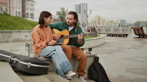 Young Busker Couple Sitting on Bench with Guitar Writing New Song Vídeo Stock 319077110