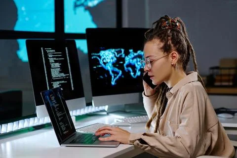 Young busy IT programmer talking on mobile phone and using laptop Stock Photos