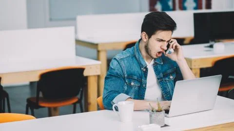 Young busy man with beard working on laptop and using mobile phone Stock Photos