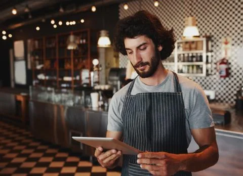 Young cafe owner checking for online order on digital tablet while standing in Stock Photos