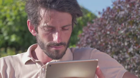 Young carefree man using a tablet while sitting in the park Stock Footage 132915973