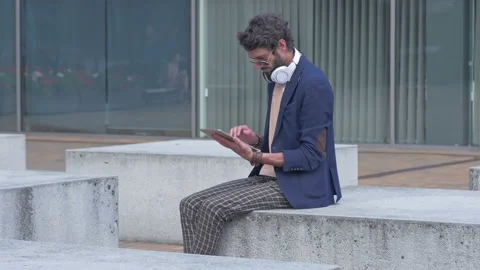 Young carefree man using a tablet while sitting on the bench Stock Footage 132933738