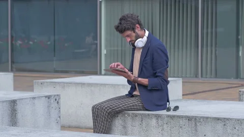 Young carefree man using a tablet while sitting on the bench Stock Footage 132934181