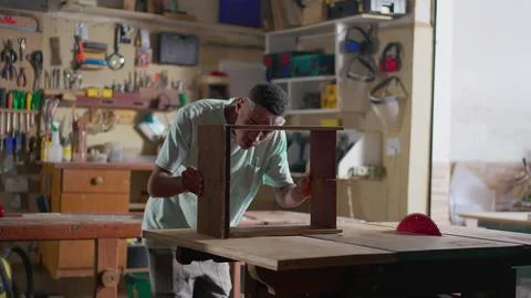 Young carpenter apprentice working at woodwork business. One black Brazilia.. Stock Photos