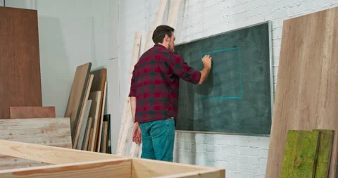 Young carpenter build a solid wood wall in a carpentry workshop. A joiner draws Stock Footage 144090065