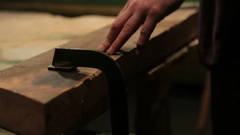 Young carpenter locks a block of wood to his workbench with two clamps. Stock-Footage 100761119
