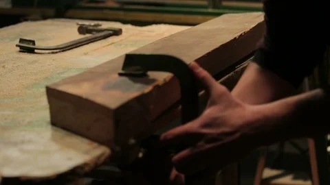 Young carpenter locks a block of wood to his workbench with two clamps. Stock-Footage 100762090