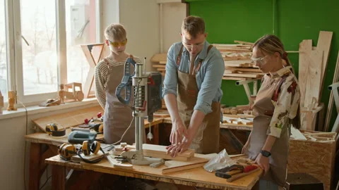 Young Carpenter Showing Two Adolescent Kids How to Use Drilling Machine Stock Footage 334431541