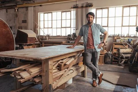 Young carpenter standing by a table in his woodworking shop Stock Photos