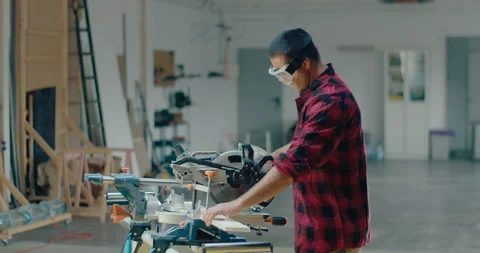 Young carpenter using an electric circular saw to cut a wood plank in home Stock Footage 199615706