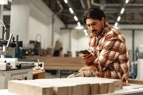 Young carpenter using his mobile phone in workshop Stock Photos