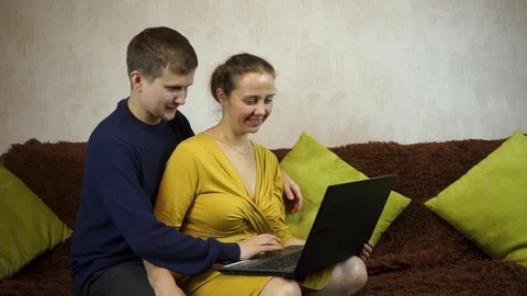 Young casual couple using laptop sitting on couch at home, Stock Footage 99403297