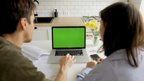 Young casual couple using laptop with green screen and sitting at home kitchen Stock Footage 127704568
