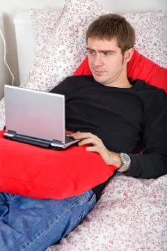 Young casual man working with computer in bed Stock Photos