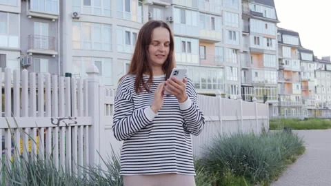 Young casually dressed female is using smartphone on a street while walking pass Vidéo 291319535