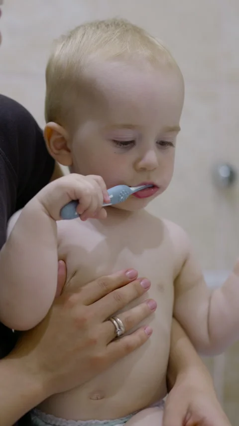Young Caucasian boy brushing teeth with blue toothbrush while being held by Stock Footage 341525088