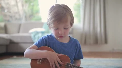 Young Caucasian boy learns to play ukulele or guitar 스톡 동영상 131349685
