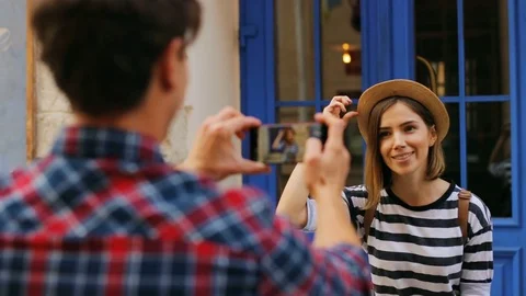 A young caucasian boy taking photo of his pretty girlfriend outside on the blue Stock Footage 80798329