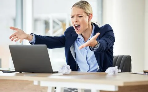 A young caucasian businesswoman yelling while using a laptop in an office at Stock Photos