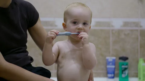 Young Caucasian child brushes teeth with blue toothbrush while seated on a Stock Footage 341896878