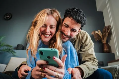 Young caucasian couple smiling using a cellphone to do shopping online. Man and Stock Photos