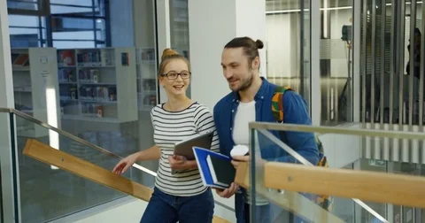 Young Caucasian couple of students walking up the stairs and talking joyfully in Stock Footage 83717367