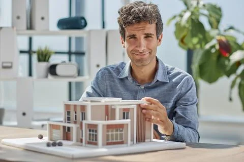 Young caucasian engineer man making building model with the use of drawings and Fotos de archivo
