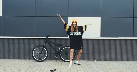 Young Caucasian female dancing near a bicycle against grey wall background Stock Footage