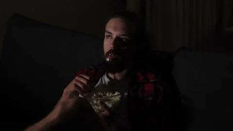 Young caucasian guy with beard wathcing tv and eating popcorn Stock Footage 159546731
