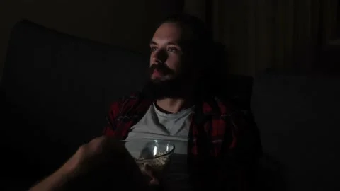 Young caucasian guy with beard wathcing tv and eating popcorn Stock Footage 159546786