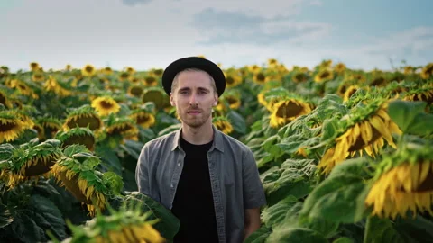 Young caucasian guy in black hat in a sunflower field on a sunny day Video stock 163231883