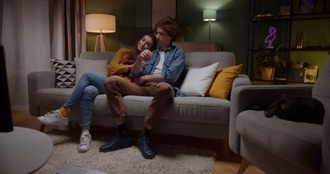 Young Caucasian guy hugging his girlfriend while they sitting on the sofa in the Stock Footage 122500652