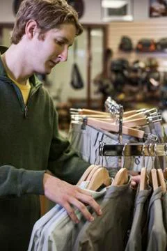 Young caucasian male checking out new shirts for sale in a fly fishing shop. Stock Photos