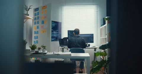 Young Caucasian male programmer writes code using multiple screens in office. Vidéo 344036013