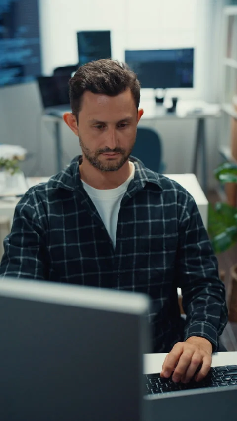 Young Caucasian male programmer writes code using multiple screens in office. Vidéo 344037348