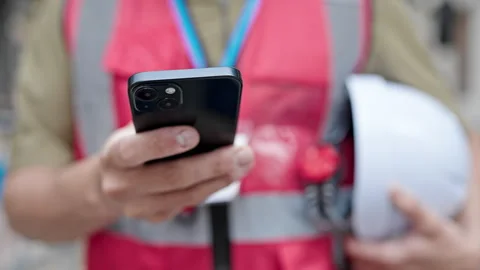 Young caucasian man architect using smartphone holding hardhat at construct.. Video stock 246144979