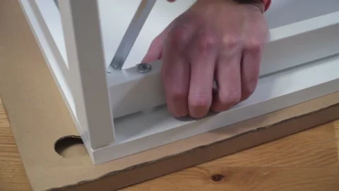 Young Caucasian man assembles white furniture from flat box using instructions Stock Footage 150771638