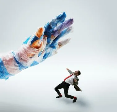 Young caucasian man avoiding big plastic hand on white studio background Stock Photos