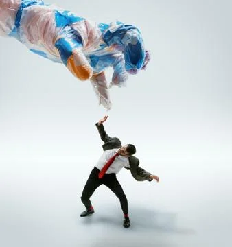 Young caucasian man avoiding big plastic hand on white studio background Stock Photos